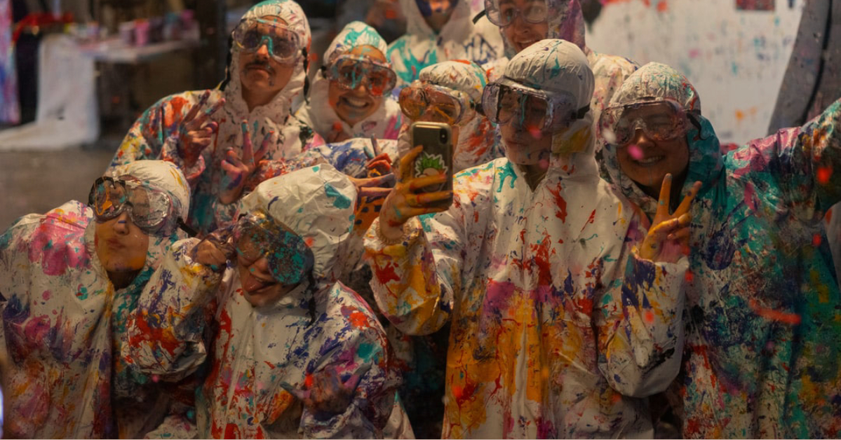 Group of people wearing safety glasses and coveralls and covered in paint splatter